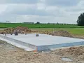 Solidna płyta fundamentowa, gotowa na budowę. Wokół piasek i zielone pola.