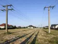 Linia 750kV przecina spokojną wieś, gdzie nowoczesne domy sąsiadują z potężnymi słupami energetycznymi.