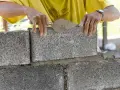 Murarz układa bloczek betonowy, sprawdzając jego wymiary.
