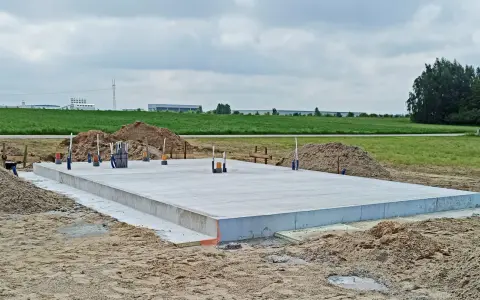Solidna płyta fundamentowa, gotowa na budowę. Wokół piasek i zielone pola.