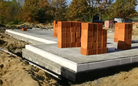 Budowa domu: betonowy fundament, bloczki, palety cegieł. Zastanawiasz się, ile kosztują fundamenty? Oto początek inwestycji.