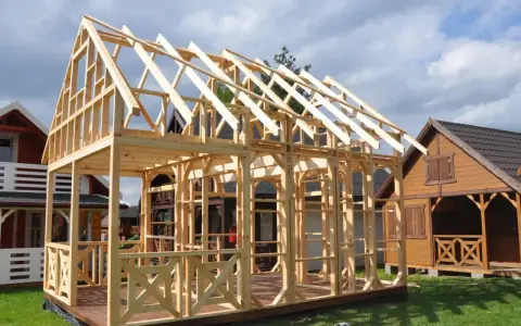 Drewniany projekt domu szkieletowego w budowie. Widać konstrukcję ścian i dachu, taras oraz balustrady.