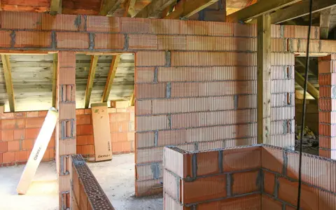 Budowa domu w trakcie. Widać ściany z pustaków ceramicznych, drewniane belki stropowe. Murowanie na piankę wady mogą pojawić się przy niedokładnym wykonaniu.