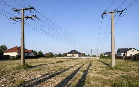 Linia 750kV przecina spokojną wieś, gdzie nowoczesne domy sąsiadują z potężnymi słupami energetycznymi.