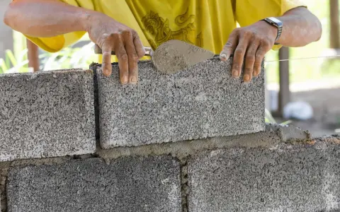 Murarz układa bloczek betonowy, sprawdzając jego wymiary.