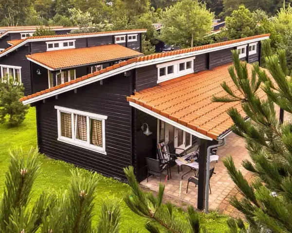 Czarny bungalow z pomarańczowym dachem, otoczony zielenią. To idealne miejsce na wypoczynek, co to znaczy bungalow?