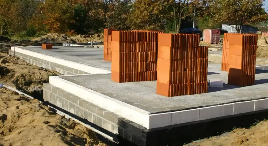 Budowa domu: betonowy fundament, bloczki, palety cegieł. Zastanawiasz się, ile kosztują fundamenty? Oto początek inwestycji.