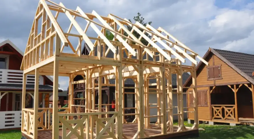 Drewniany projekt domu szkieletowego w budowie. Widać konstrukcję ścian i dachu, taras oraz balustrady.