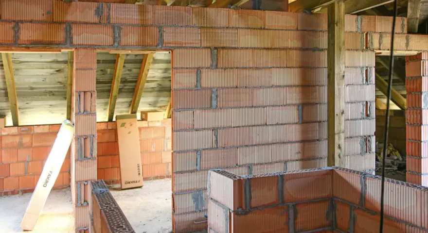 Budowa domu w trakcie. Widać ściany z pustaków ceramicznych, drewniane belki stropowe. Murowanie na piankę wady mogą pojawić się przy niedokładnym wykonaniu.