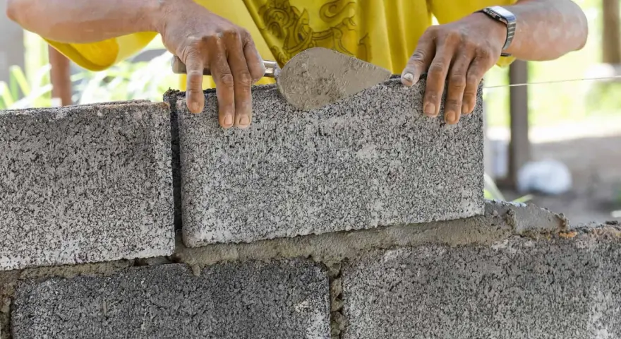 Murarz układa bloczek betonowy, sprawdzając jego wymiary.