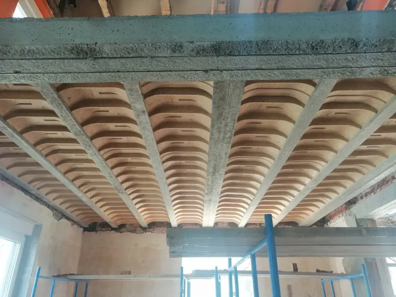 Widok od dołu na betonowe belki i pustaki, tworzące różne rodzaje stropów. Konstrukcja w trakcie budowy.