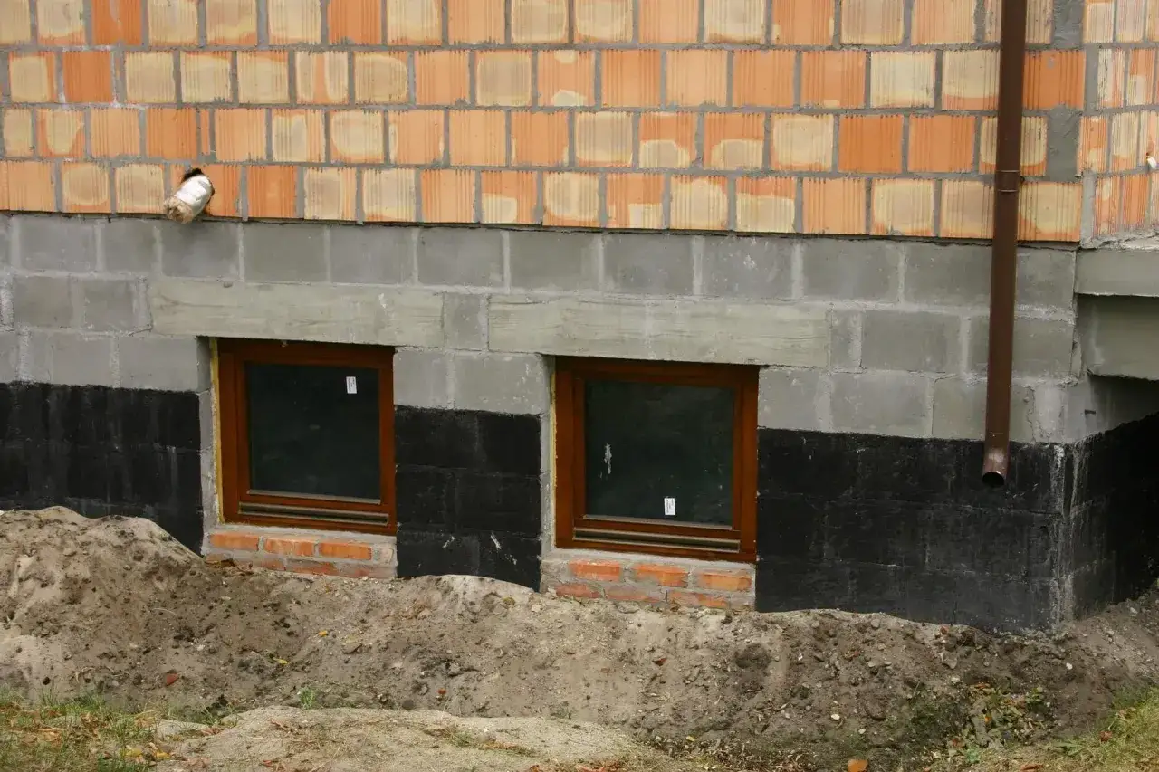 Wzmocnienie fundamentów w starym domu: nowe okna piwniczne, izolacja i drenaż.