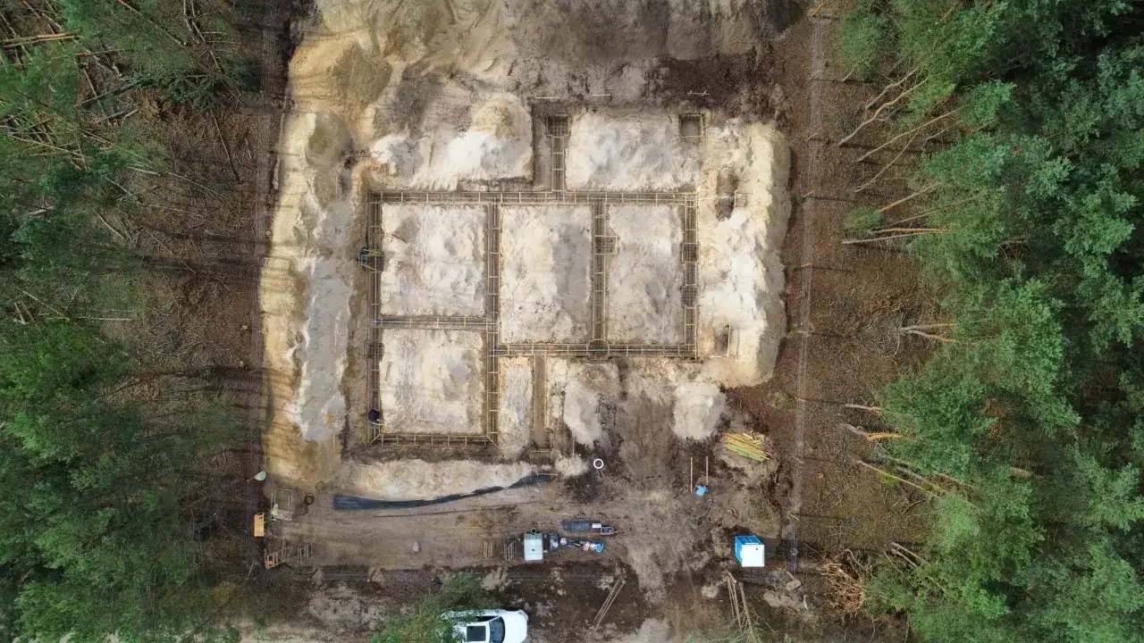 Budowa fundamentów domu w lesie. Widać wykop, zbrojenie i szalunki. To przykład praktycznego zastosowania wiedzy o geologii.