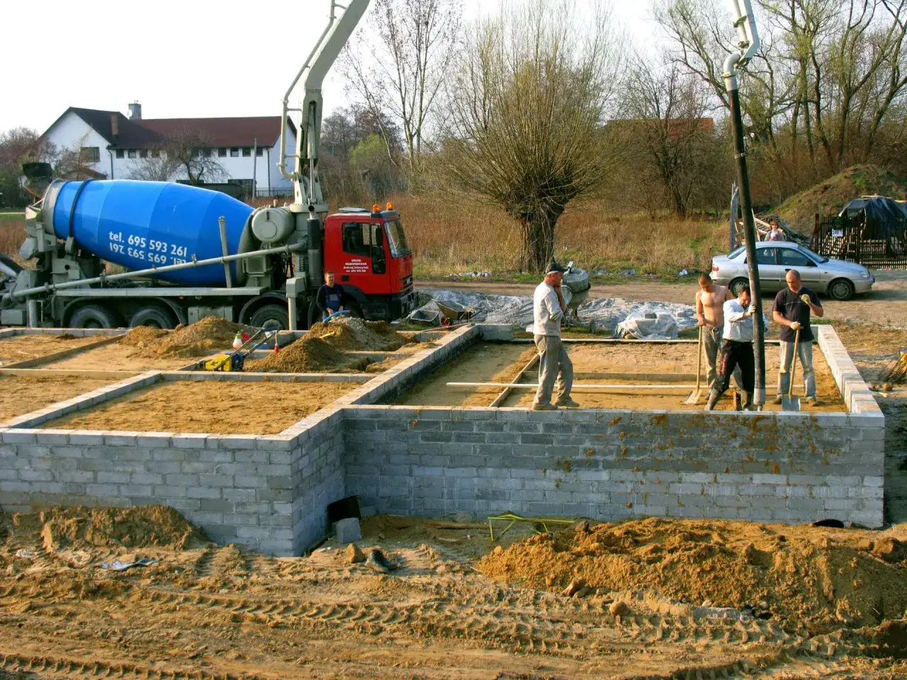 Budowa fundamentów: betoniarka i ekipa przygotowują teren. Czym obsypać fundamenty z zewnątrz? Piaskiem i ziemią.