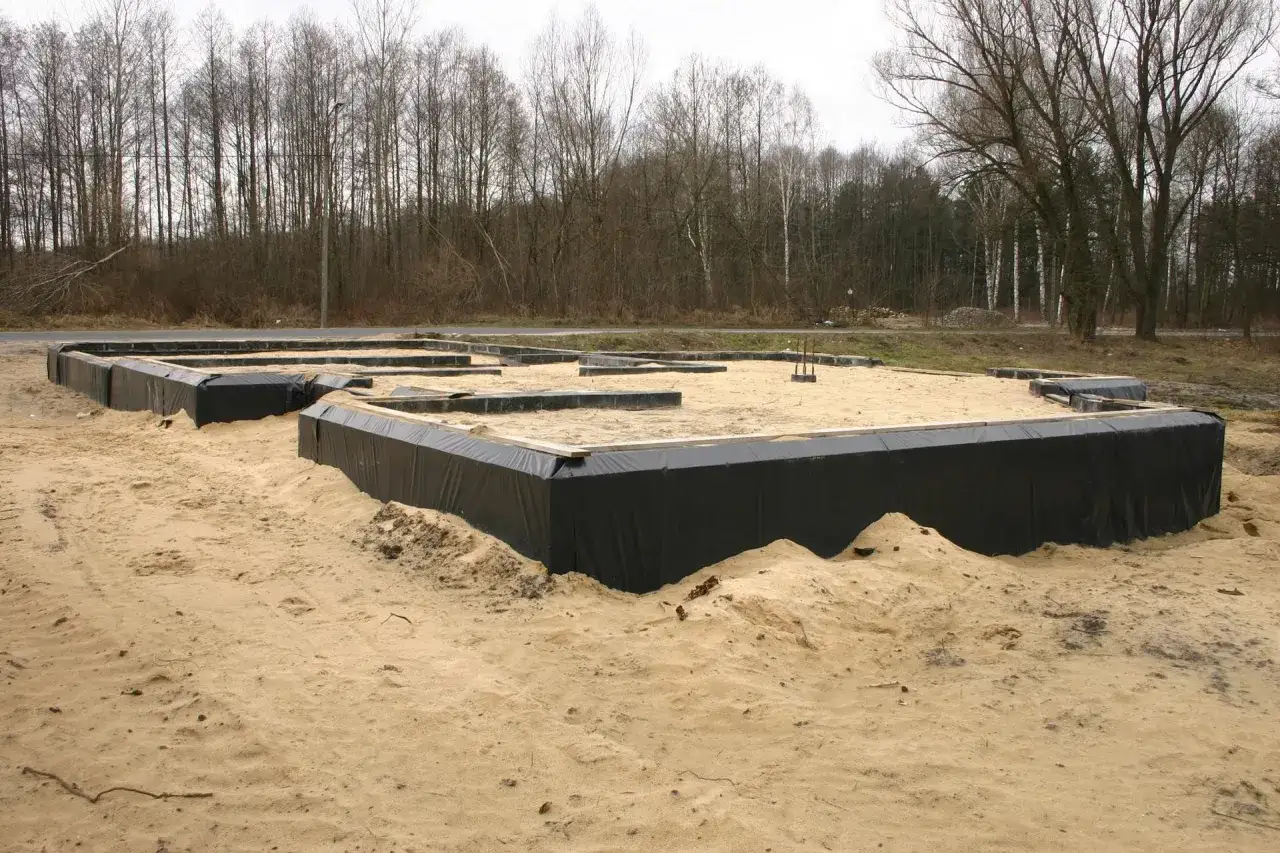 Fundament domu w piasku, otoczony czarną folią. W tle las. To nie styropian, to fundament z wykorzystaniem styrobetonu.